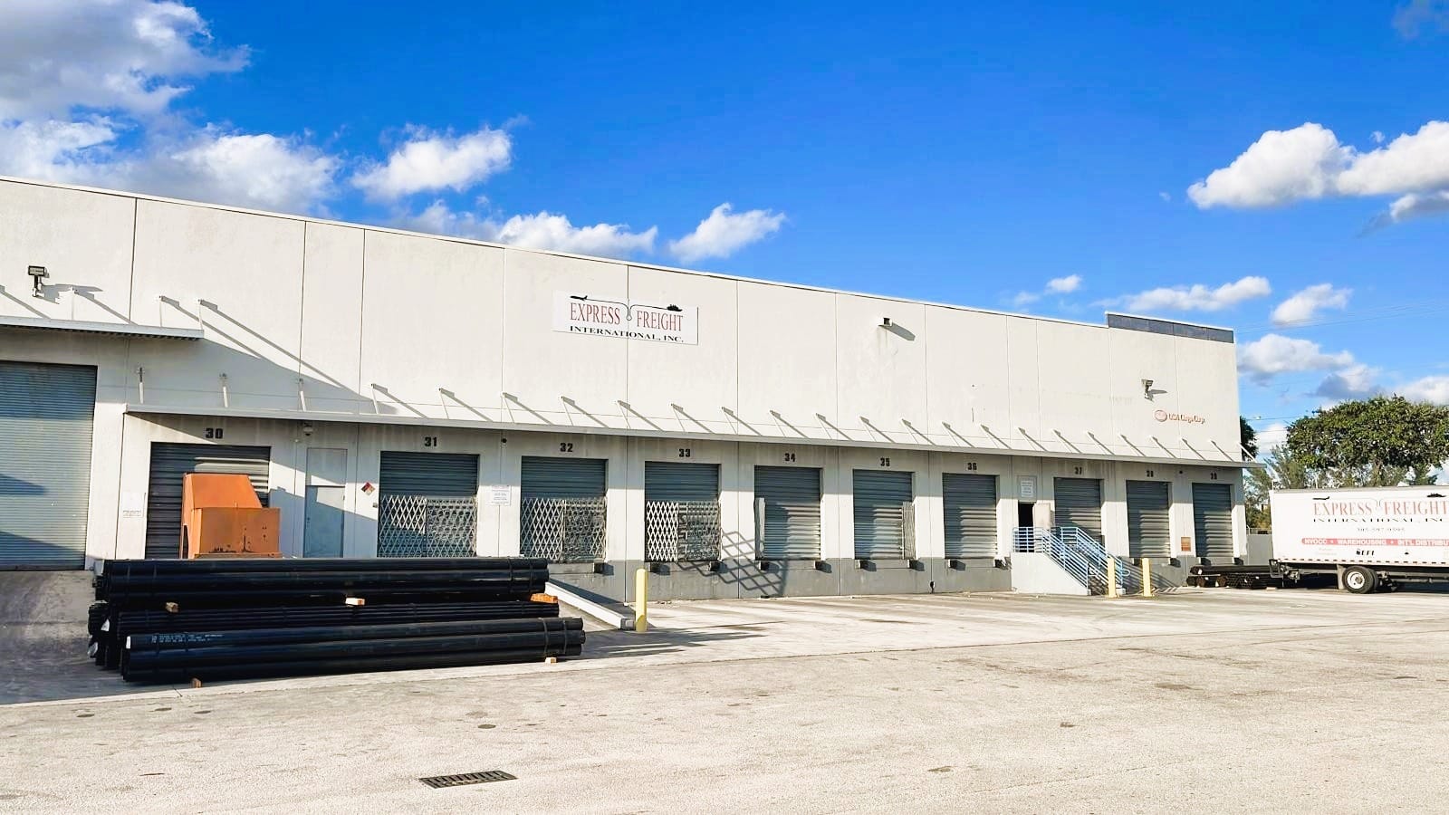 The loading dock at Express Freight International in Medley, Miami: a run of numbered dock doors along the warehouse with export cargo staged on the apron