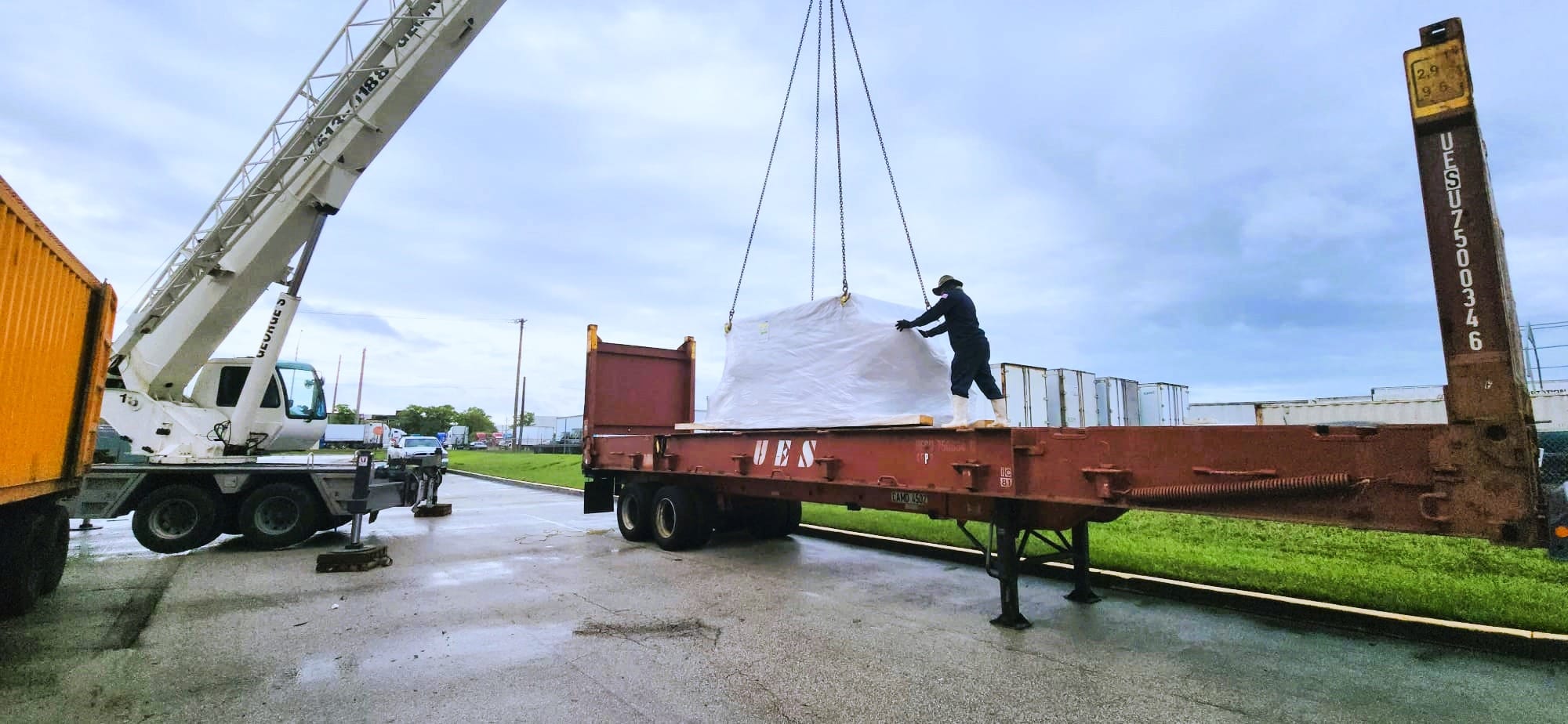 Crane lowering a wrapped oversize load onto a flat rack trailer at the Express Freight International facility in Miami