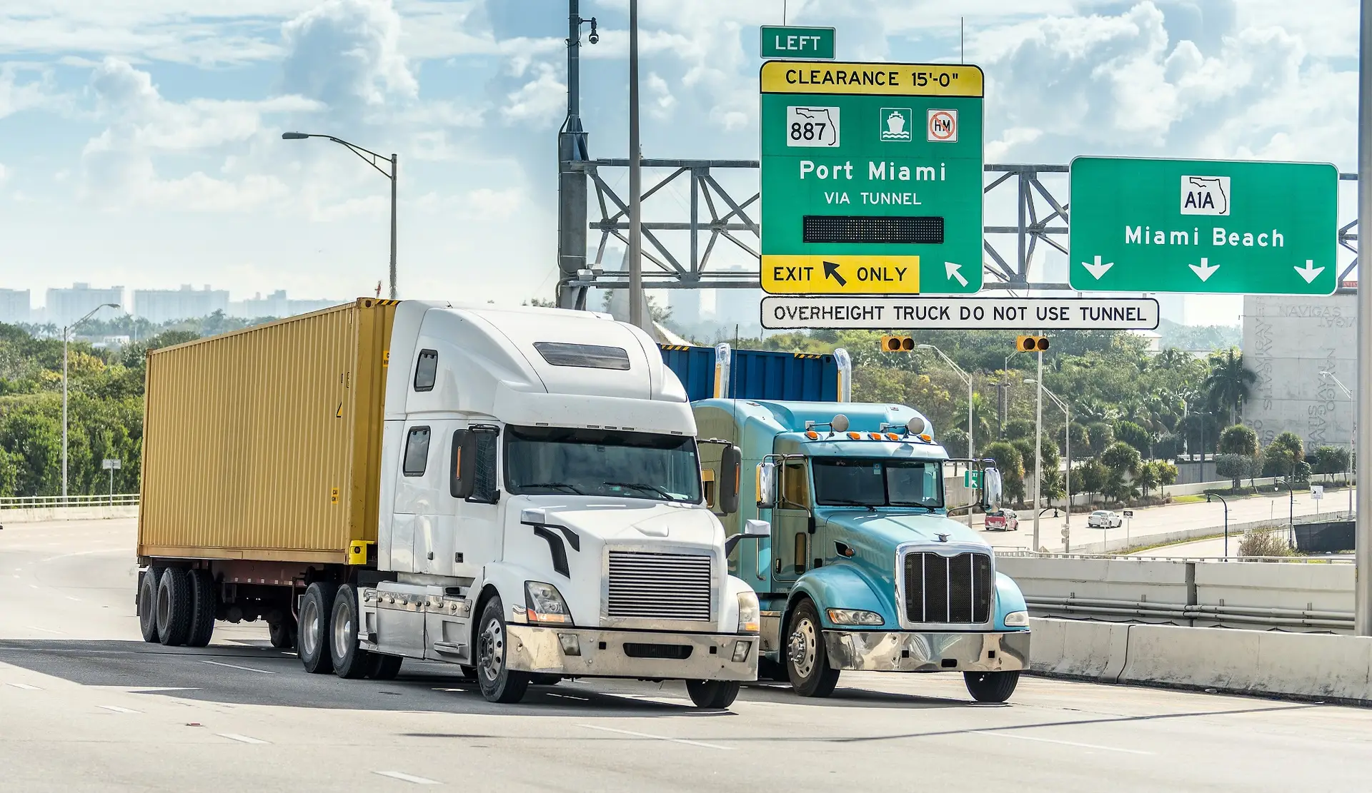 Camiones con contenedores en la aproximación por carretera a PortMiami bajo señalización aérea