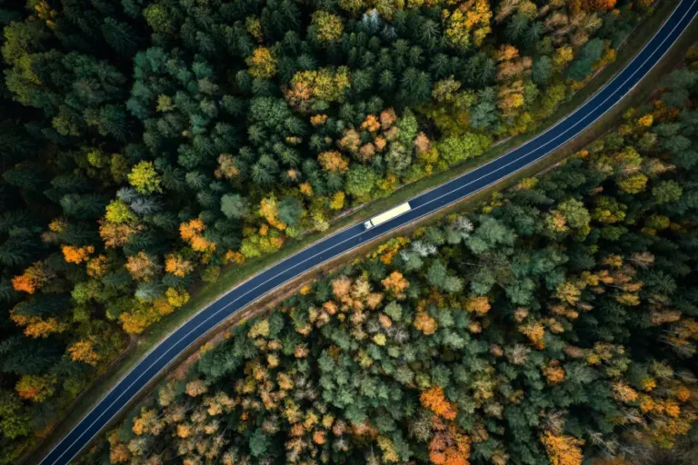 Aerial view of a heavy truck on a winding road lined with autumn trees