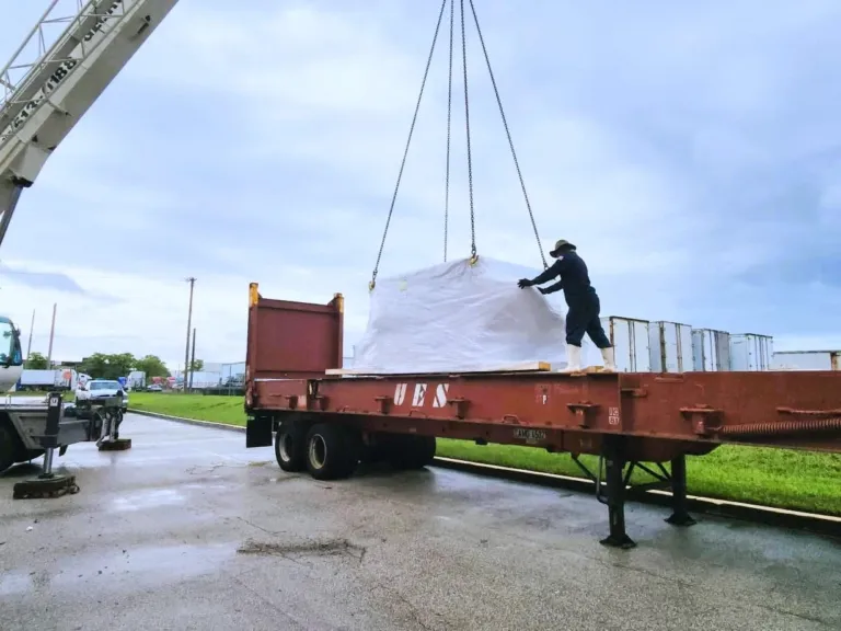A crane lowering a wrapped oversize load onto a flat rack trailer in the EFI yard