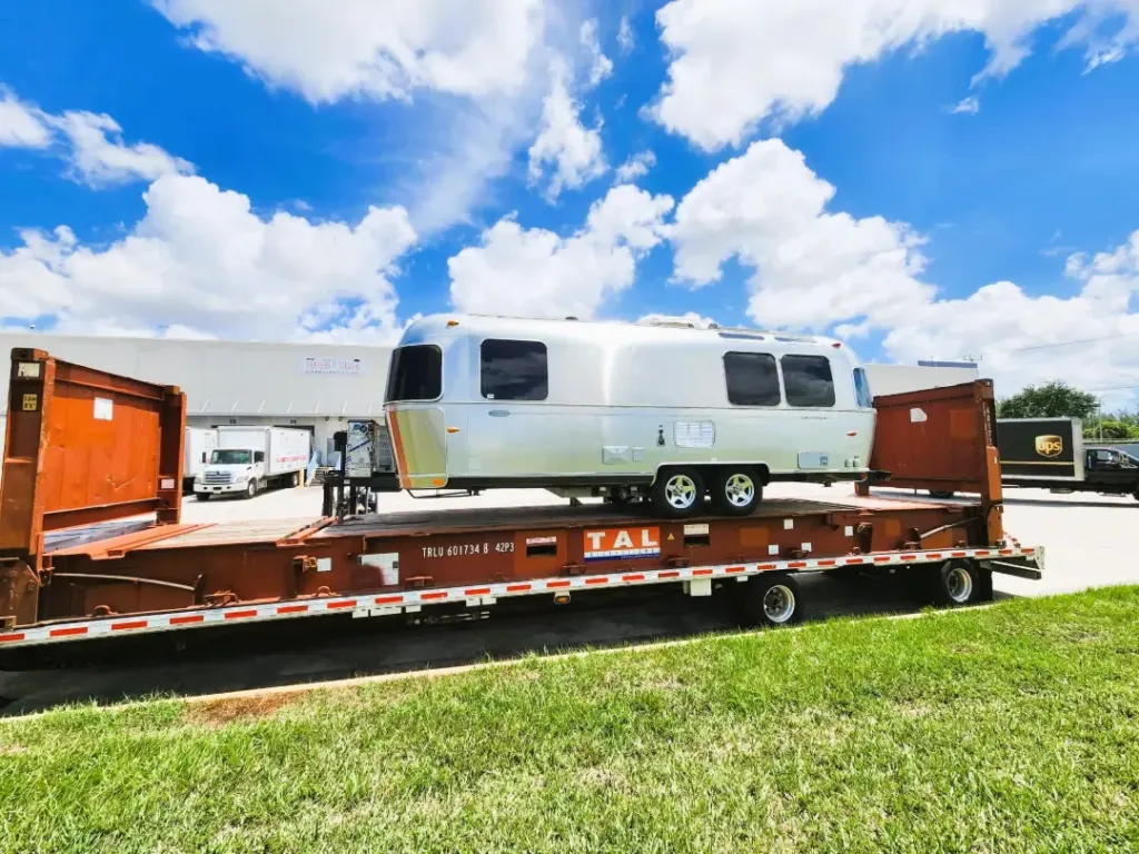 An Airstream travel trailer loaded onto a flat rack container on a step-deck trailer.