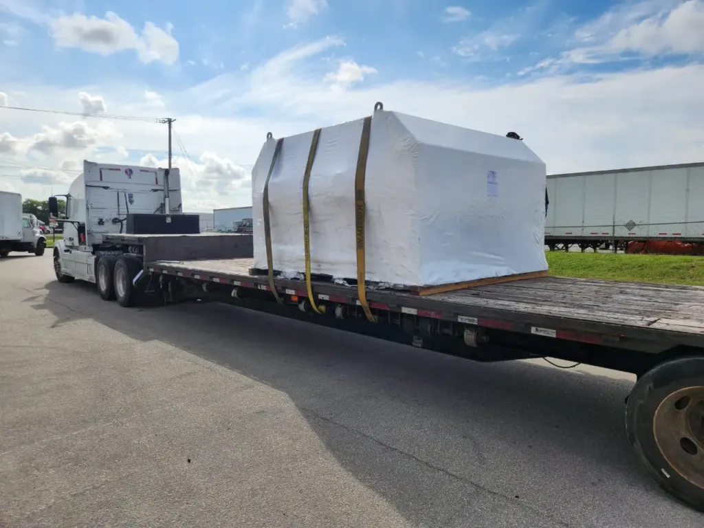 A large crated machine strapped to a flatbed trailer outside the EFI warehouse in Miami, staged for air freight