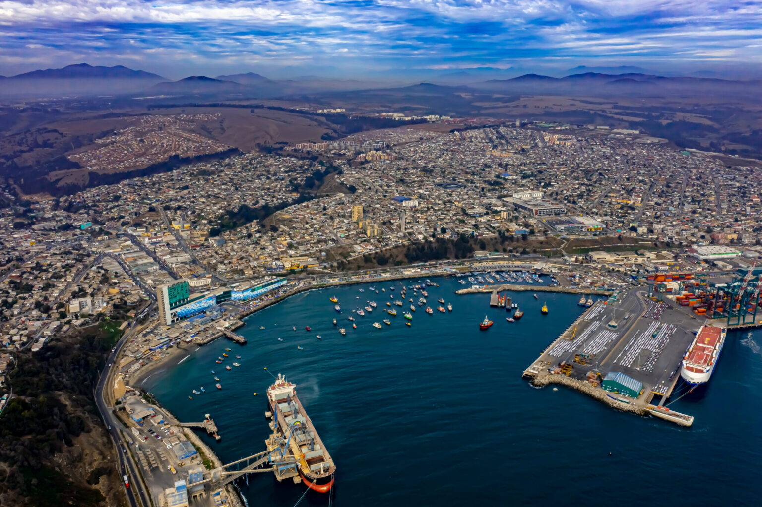 Aerial view of the Port of San Antonio, Chile, with a car carrier at the terminal, container cranes and the town on the hills behind